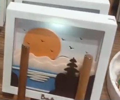 White 3D frame with an orange sunset, birds, layered clouds, a blue sea and a Balinese temple silhouette