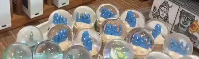 Rows of small glass snow globes with blue 3D letters on a sandy base